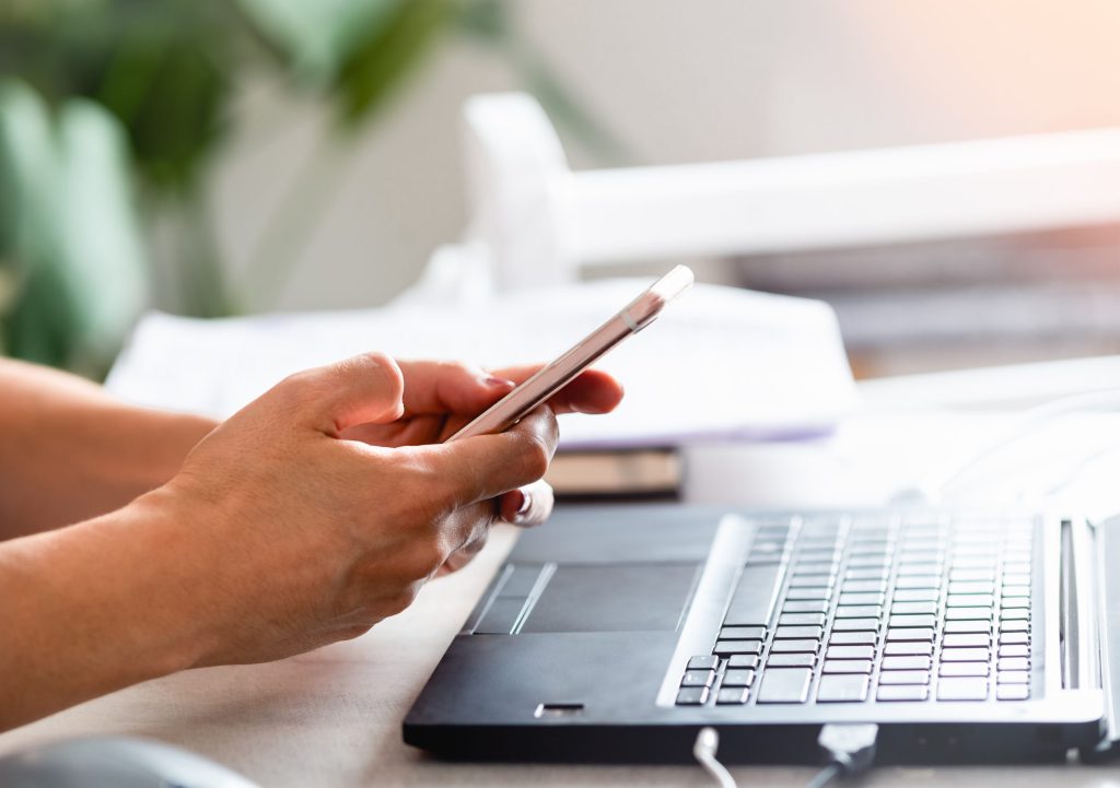 Woman watching cell phone while working on computer.