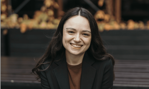 Sophie Cusworth smiling, wearing brown shirt and black blazer. She has light skin and long dark brown hair